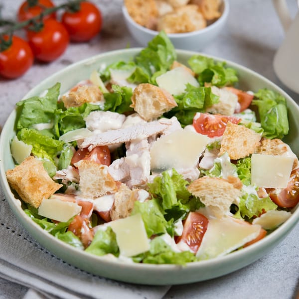 A fresh Caesar salad with chicken, croutons, parmesan, and cherry tomatoes in a green bowl.