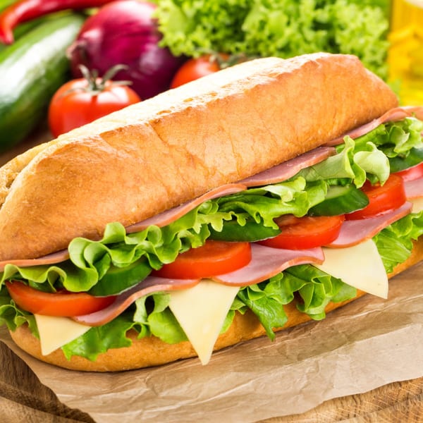 A large submarine sandwich filled with ham, cheese, lettuce, tomatoes, and cucumbers on a wooden board.
