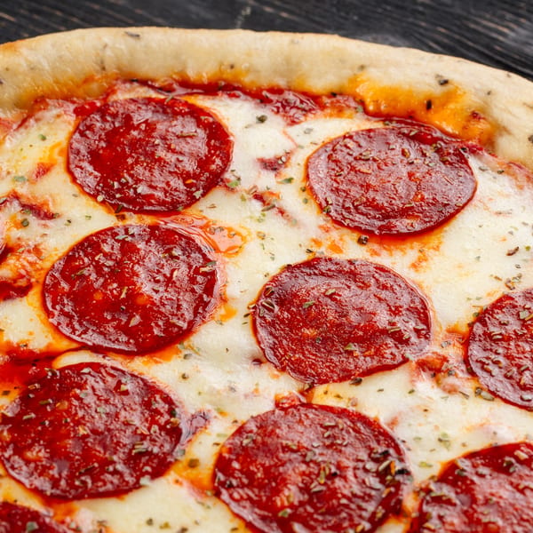 Close-up of a Holden Pizza pepperoni pizza with melted cheese and herbs on a dark surface.