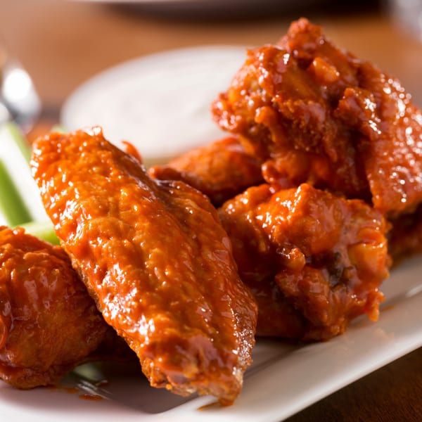 A plate of Holden Pizza's buffalo wings, coated in a glossy orange sauce, with celery and dip.